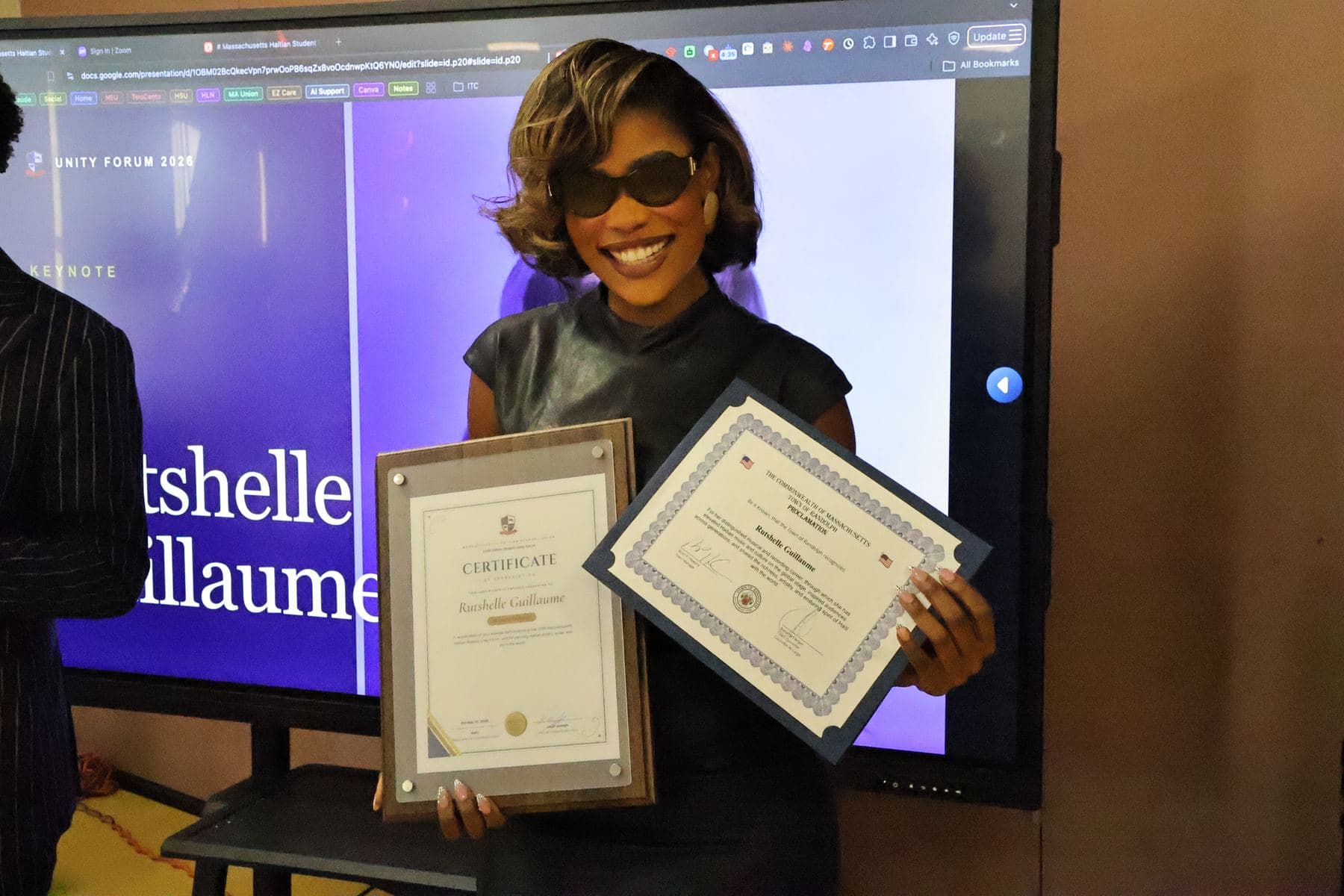 Rutshelle Guillaume holding her certificate in front of a screen with her name